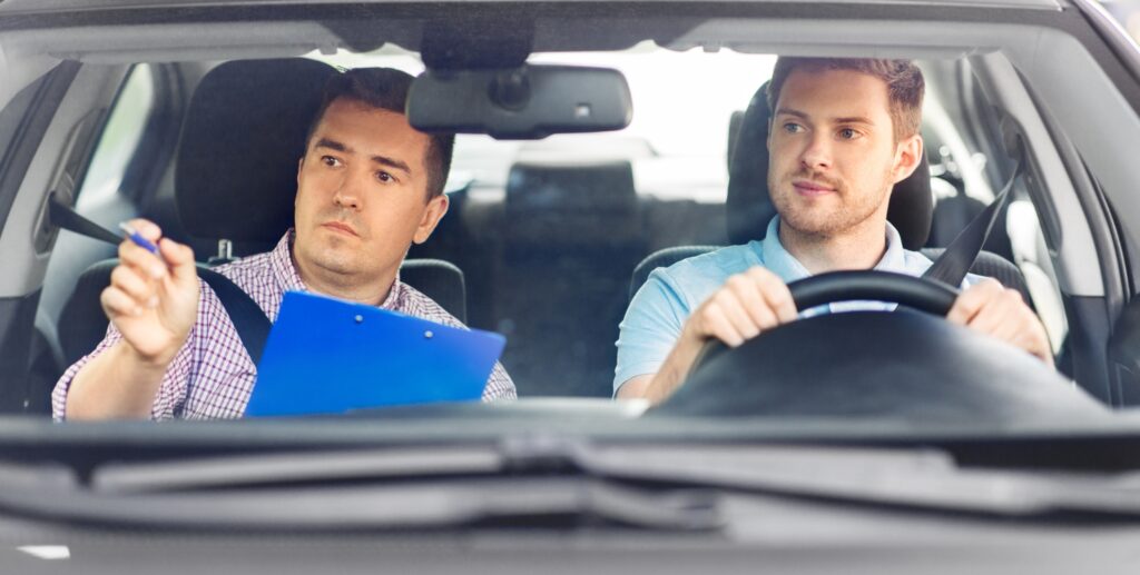 Bilde av en kjørelærer og en student i en bil under oppkjøring, kjørelæreren gir studenten tips til oppkjøring